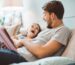Father and daughter enjoying at home. Sitting on bed and reading book together.